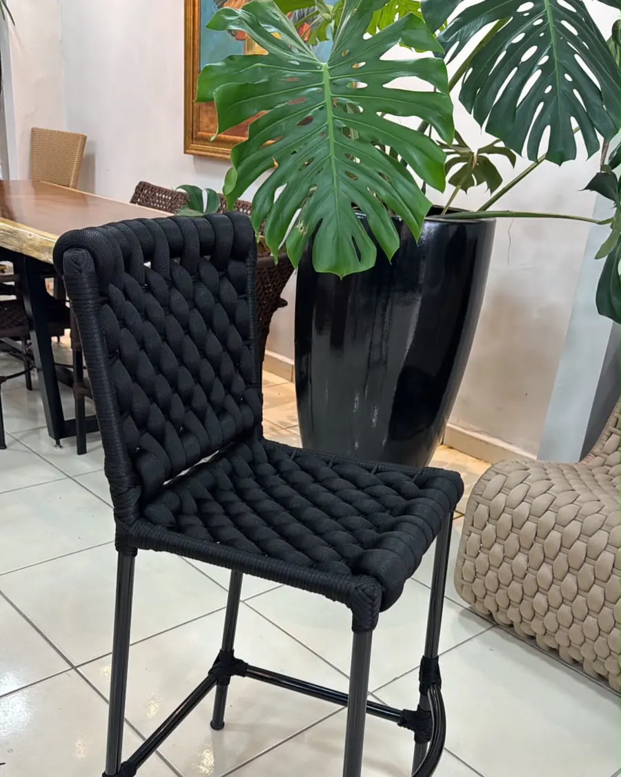 Banqueta alta com encosto em trançado preto ao lado de vaso decorativo