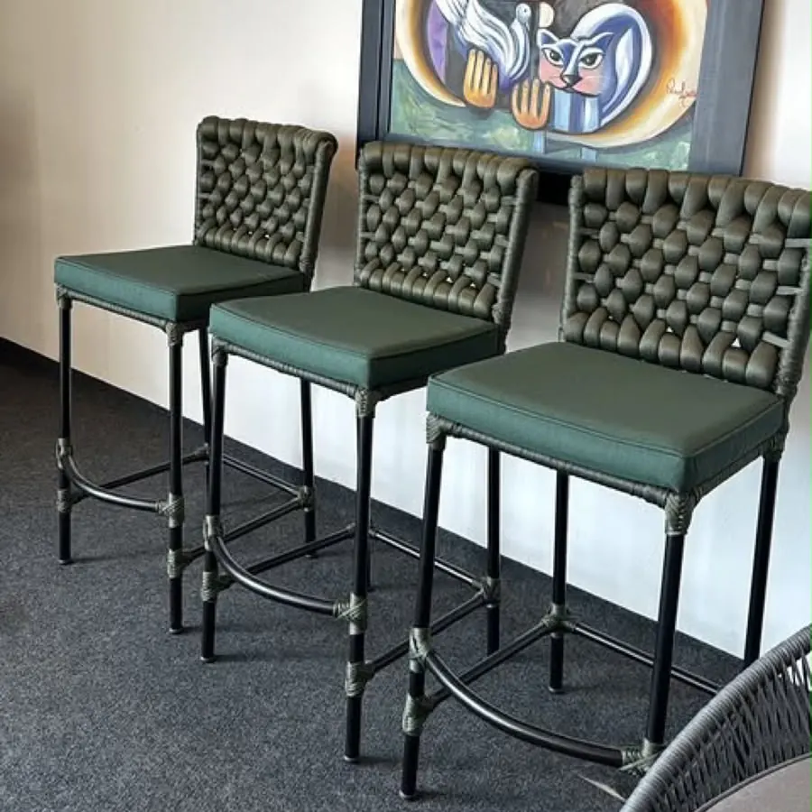 Banquetas altas com assento verde alinhadas junto à parede